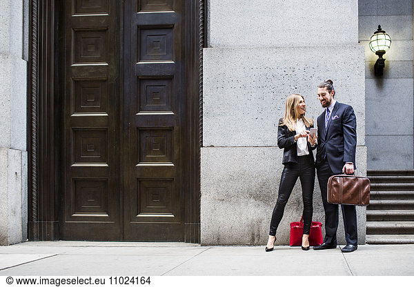 Businessman and woman looking at smart phone while standing on sidewalk