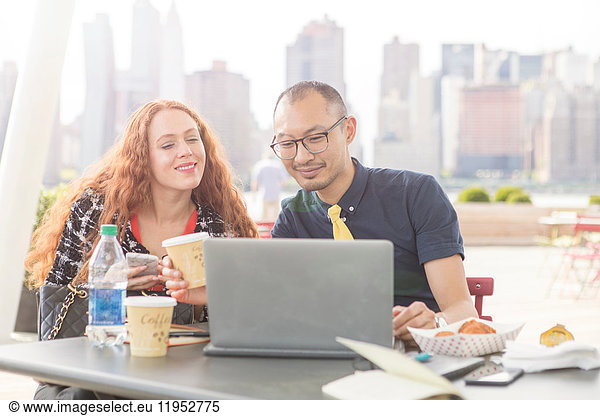 Businessman and woman using laptop at waterfront cafe table  New York  USA