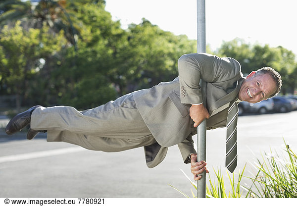 Businessman balancing on pole on city street