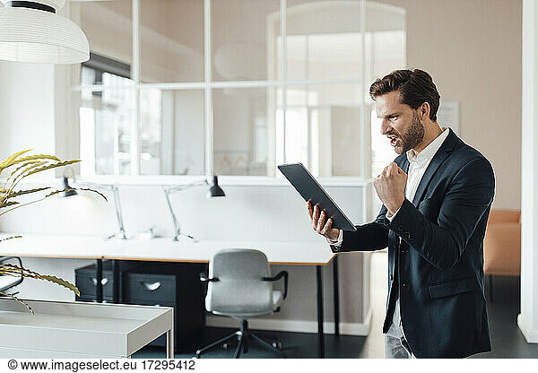 Businessman cheering while using digital tablet in office