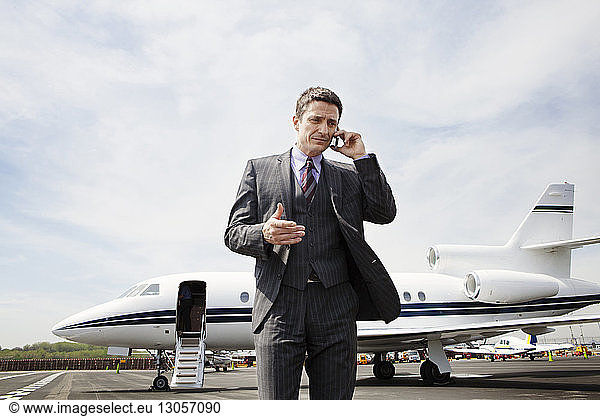 Businessman communicating on phone while standing against corporate jet on runway