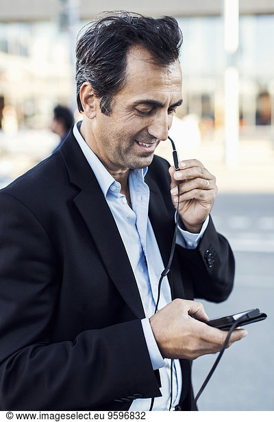 Businessman communicating through headphones while using mobile phone on street