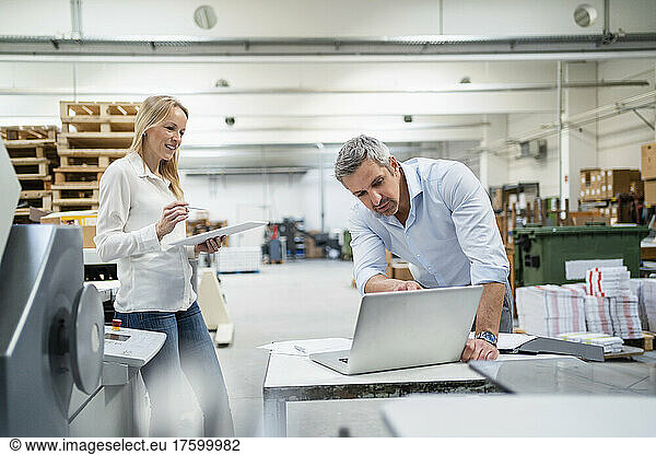 Businessman discussing ideas over laptop with colleague in factory