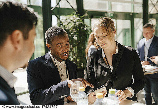 Businessman discussing with female colleague over smart phone during networking event