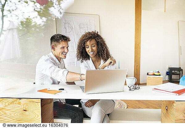 Businessman discussing with female coworker over laptop on desk in office