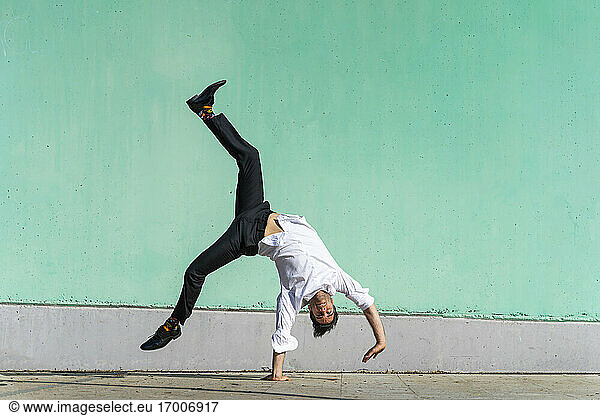 Businessman doing handspring in front of green wall