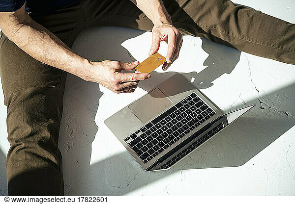 Businessman doing online shopping sitting on floor with credit card and laptop