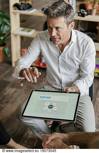 Businessman explaining a mind map on tablet screen during a presentation in loft office