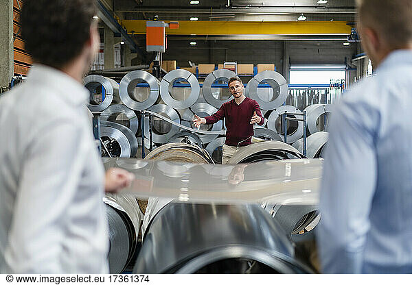 Businessman explaining colleagues while standing by rolled sheet metal at industry