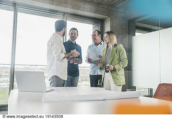 Businessman explaining to colleagues with laptop and blueprint on table