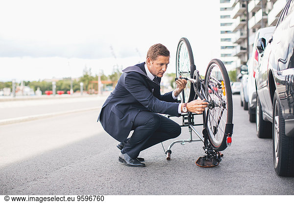 Businessman fixing bicycle chain on city street against sky