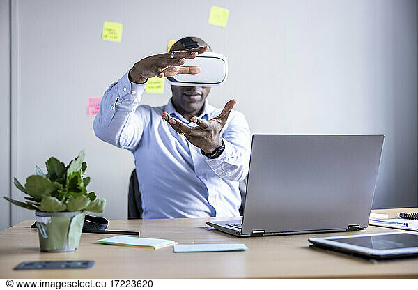 Businessman gesturing wearing Virtual reality headset while sitting at desk in office