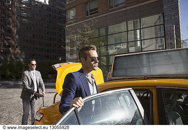 Businessman getting in taxi with colleague in background