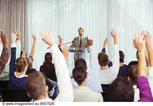 Businessman giving presentation in conference room  people raising hands
