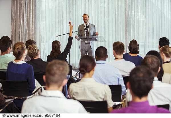 Businessman giving speech in conference room  woman from audience raising hand