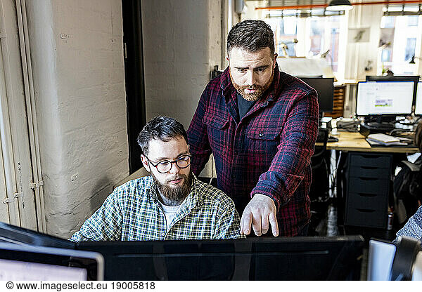 Businessman having discussion with colleague over computer in office