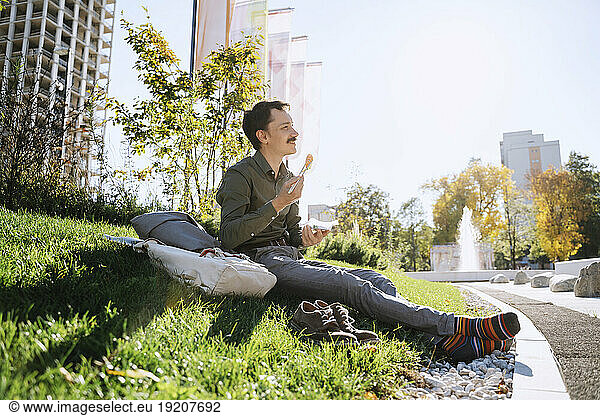 Businessman having lunch sitting on grass at office park