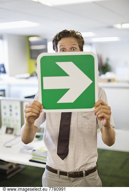 Businessman holding arrow sign in office