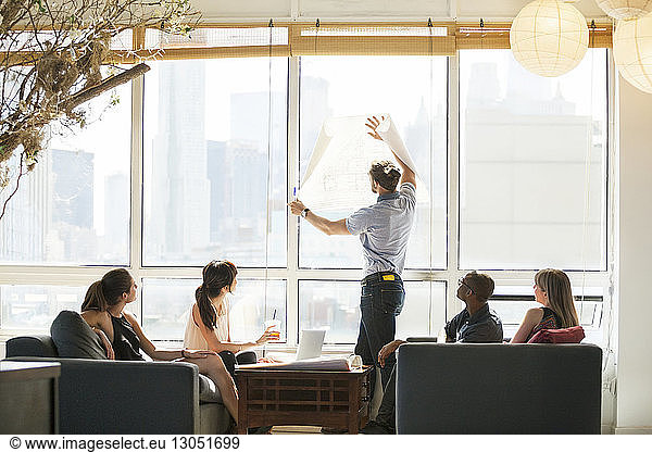 Businessman holding blueprint against window during meeting