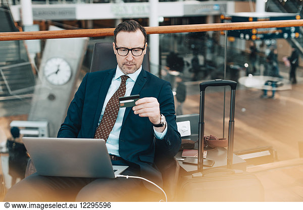 Businessman holding credit card while using laptop in airport