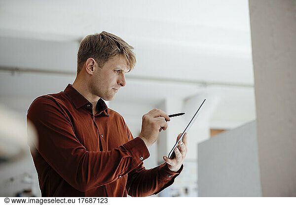 Businessman holding digitized pen using tablet PC standing in office