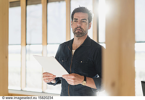 Businessman holding document in wooden open-plan office