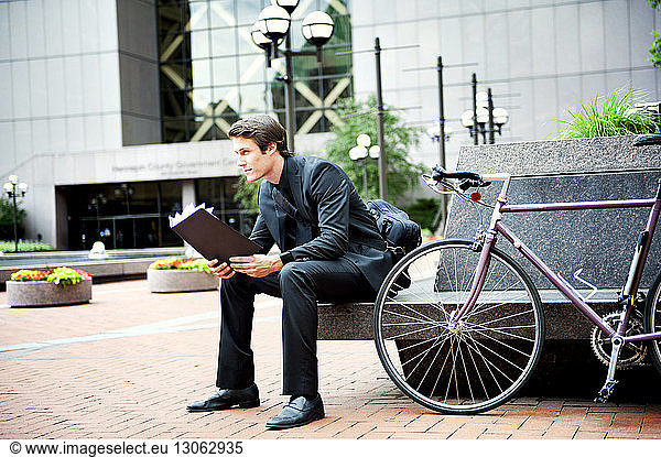 Businessman holding folder while sitting by bicycle on seat