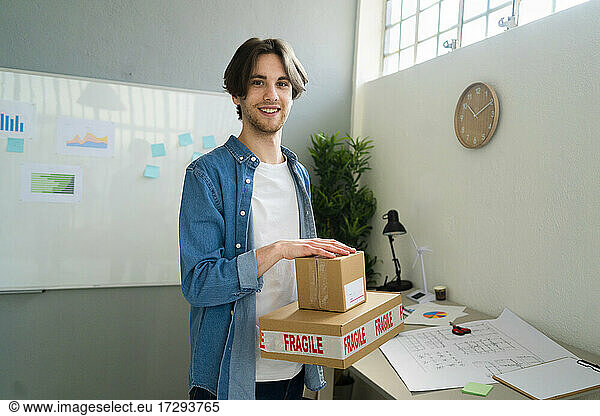 Businessman holding fragile cardboard boxes while standing at office