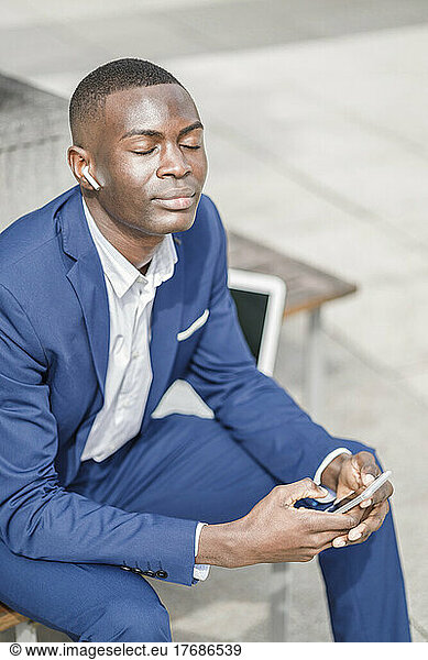 Businessman holding mobile phone listening music through wireless in-ear headphones