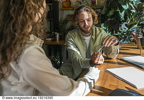 Businessman holding pen and discussing with colleague sitting at cafe