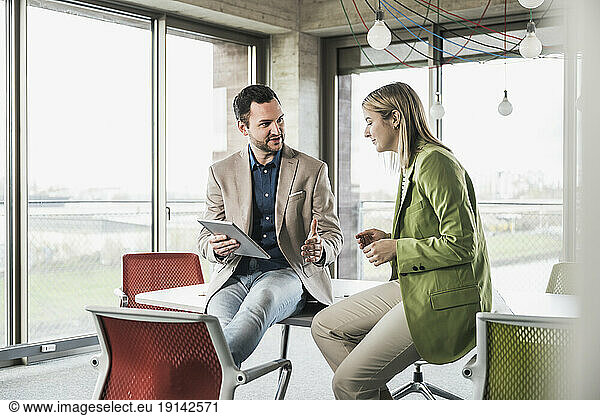 Businessman holding tablet PC discussing with coworker in office