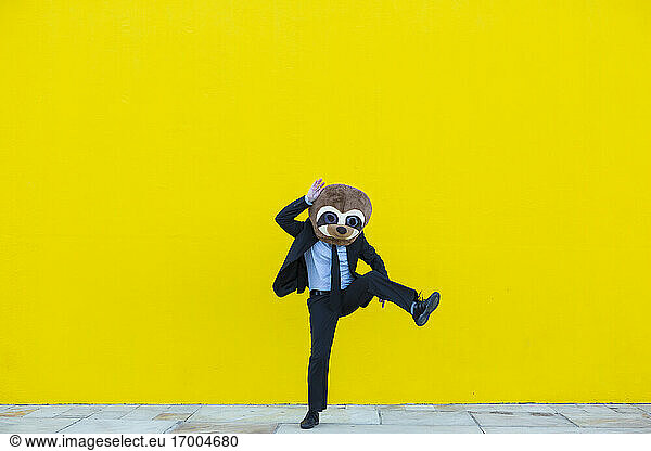 Businessman in black suit with meerkat mask dancing in front of yellow wall
