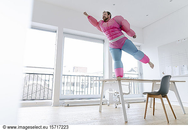 Businessman in office wearing pink bodybuilder costume pretending to fly