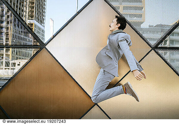 Businessman in suit jumping in front of modern office building