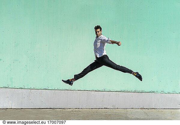 Businessman jumping in front of green wall