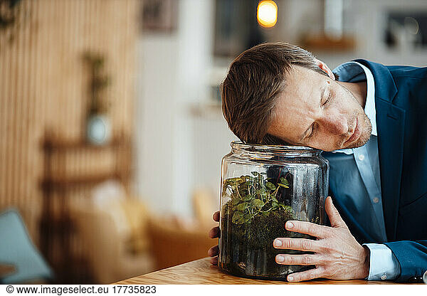 Businessman leaning on glass container with plant in cafe