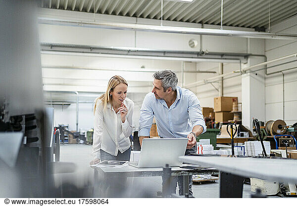 Businessman looking at colleague discussing ideas at desk in factory