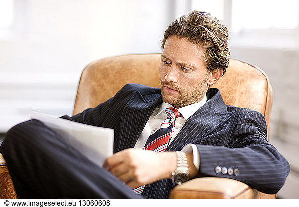 Businessman looking at document while sitting on arm chair