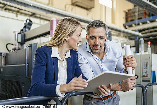 Businessman looking at tablet PC discussing with blond businesswoman in factory