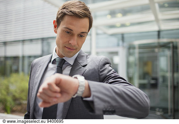 Businessman looking at watch outside office building