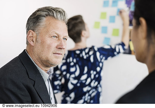 Businessman looking away while colleague reading adhesive notes at office