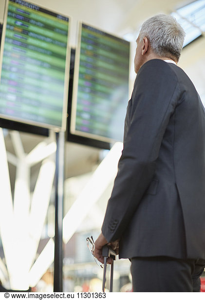 Businessman looking up at airport arrival departure board