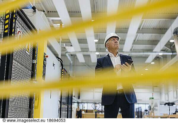 Businessman looking up holding mobile phone in factory