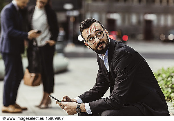 Businessman looking up while using mobile phone outdoors