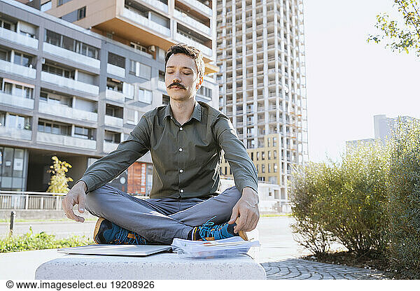 Businessman meditating sitting cross-legged at office park