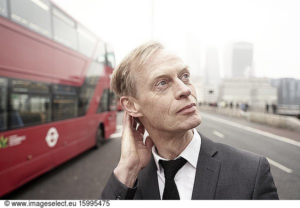 Businessman next to red double-deck bus in London  UK.