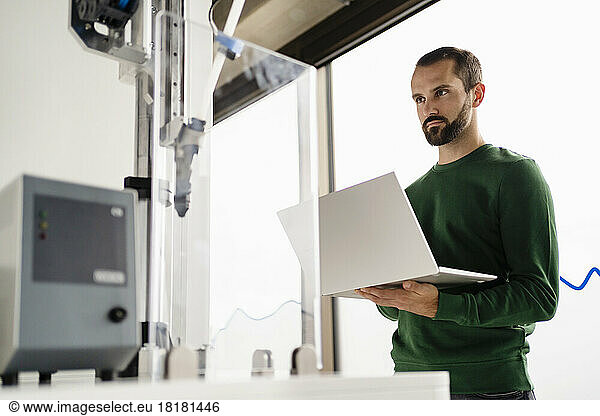 Businessman operating machine through laptop at industry