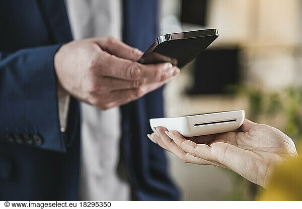 Businessman paying through mobile phone on card reader machine