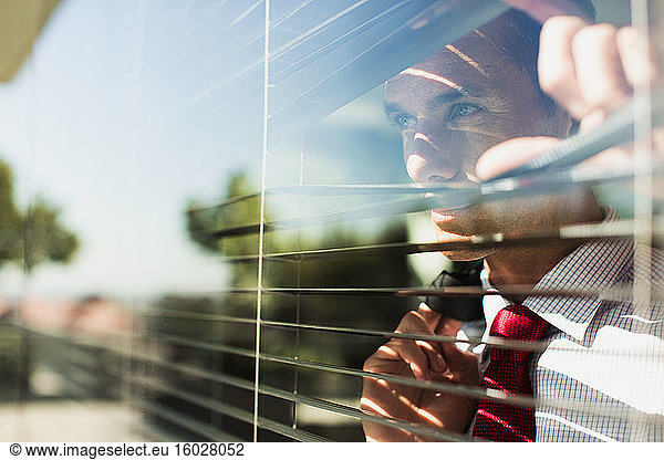 Businessman peering through window blinds