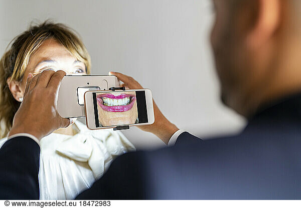 Businessman photographing colleague's smile through smart phone using magnification equipment